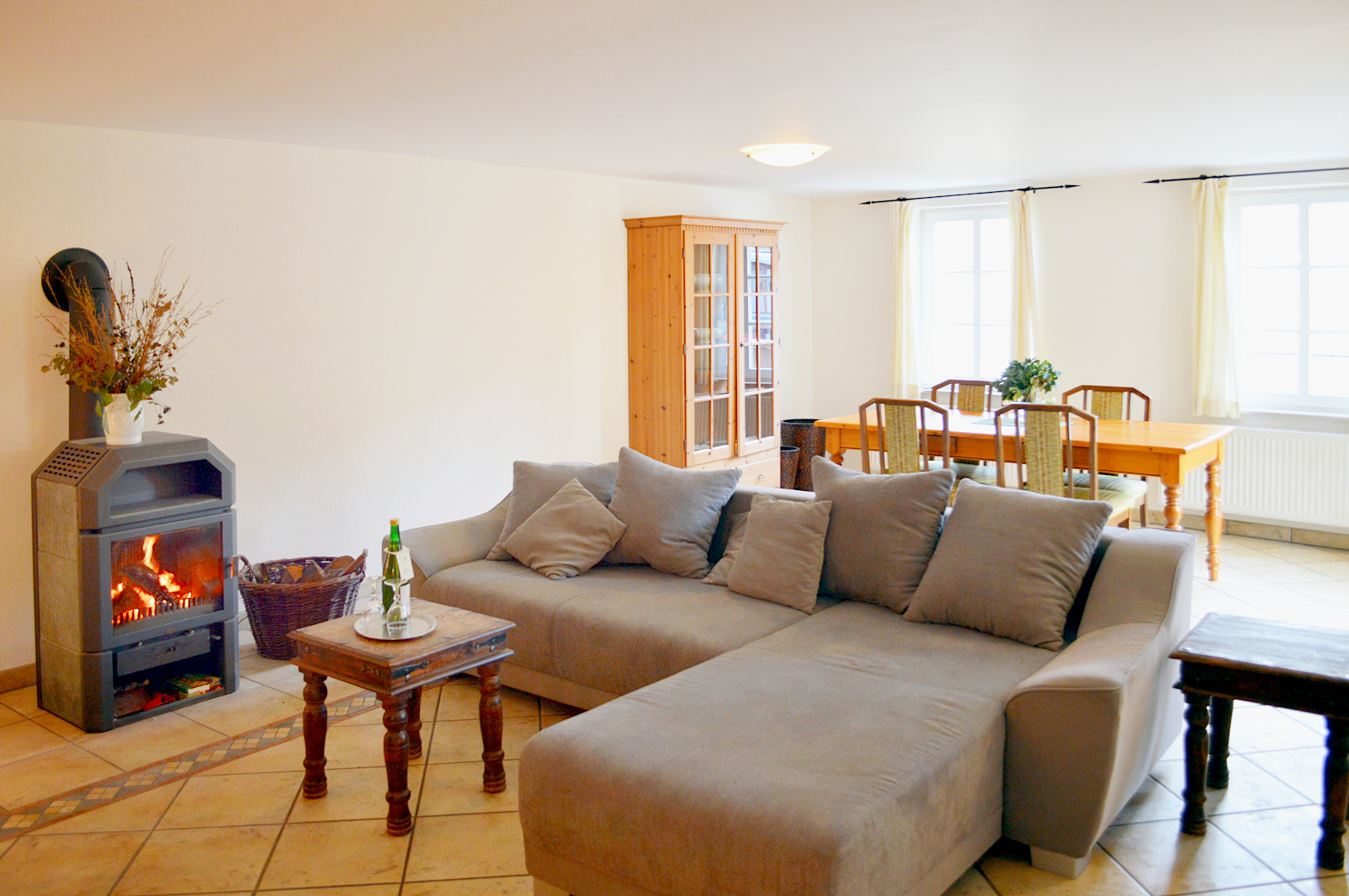 Geräumiges Zimmer mit Eck-Sofa, brennendem Specksteinofen und einem Tisch mit 4 Stühlen
